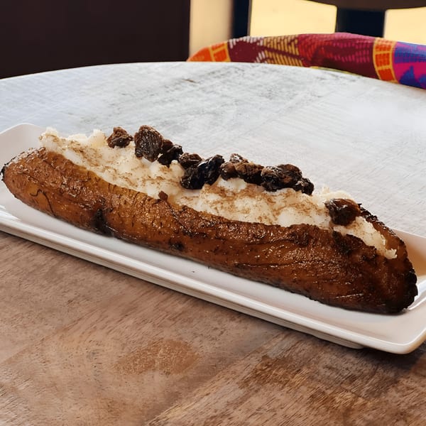 A Salvadoran dessert of a fried plantain topped with white cream, cinnamon, and raisins on a white plate.