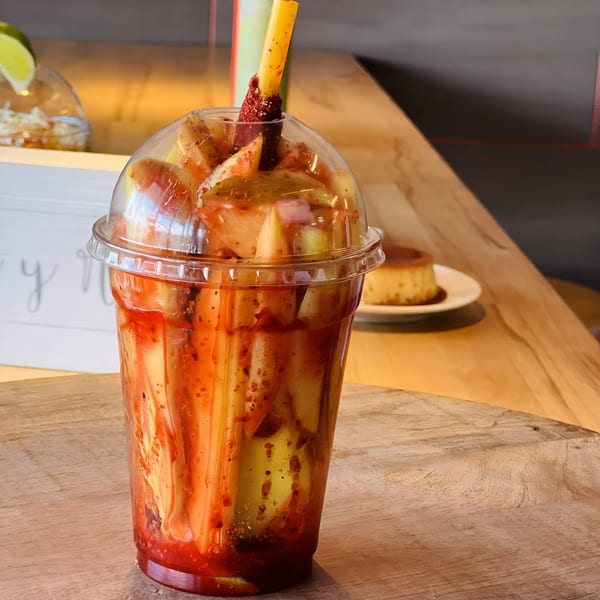 A plastic cup filled with sliced mangoes and a red chili sauce, with a tamarind candy straw.