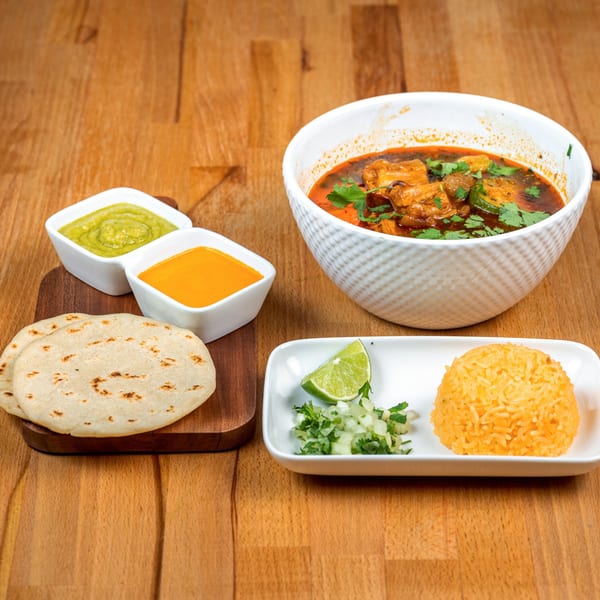 Salvadoran meal with a bowl of stew, rice, tortillas, lime, chopped onions, and two dipping sauces.