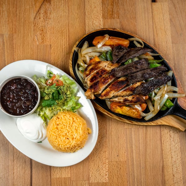 Sizzling fajitas with chicken and steak, served with rice, black beans, guacamole, and sour cream.