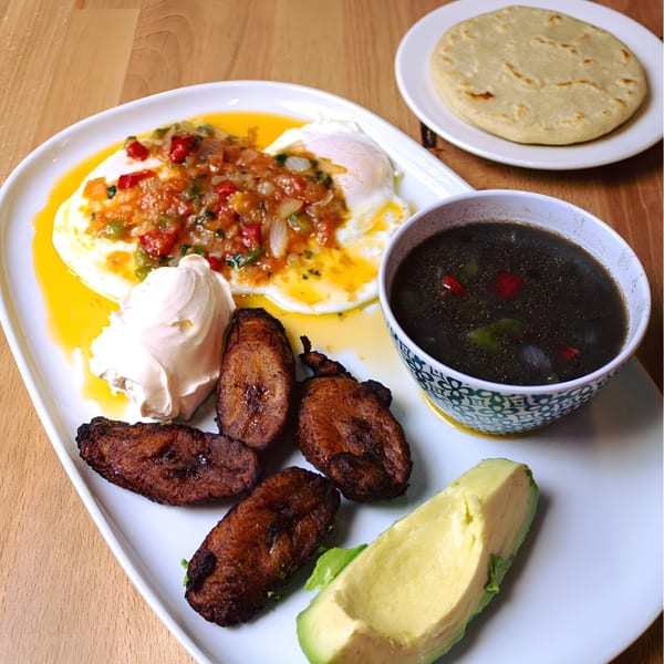 Salvadoran breakfast with fried eggs, salsa, plantains, avocado, black beans, and a tortilla.