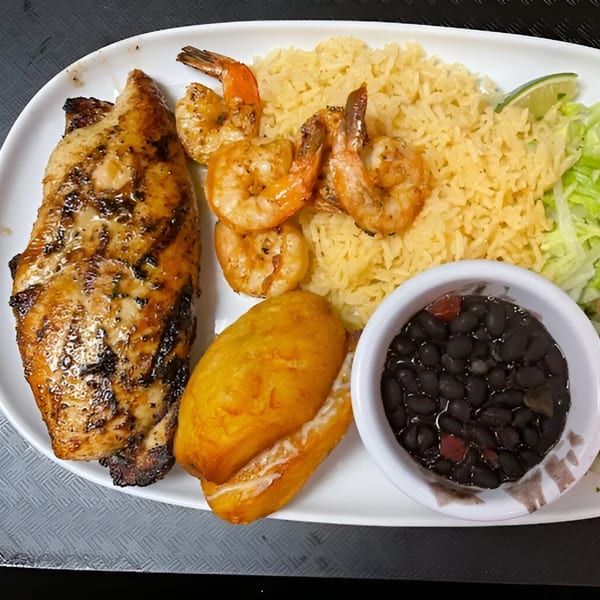 Grilled chicken and shrimp with yellow rice, fried plantain, black beans, and lime on a white plate.